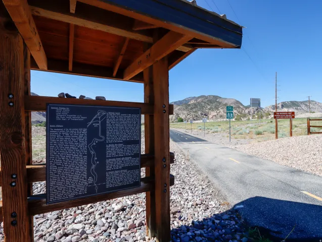 Outdoor informational sign with a wood-finish frame and metal roof, set on a gravel base