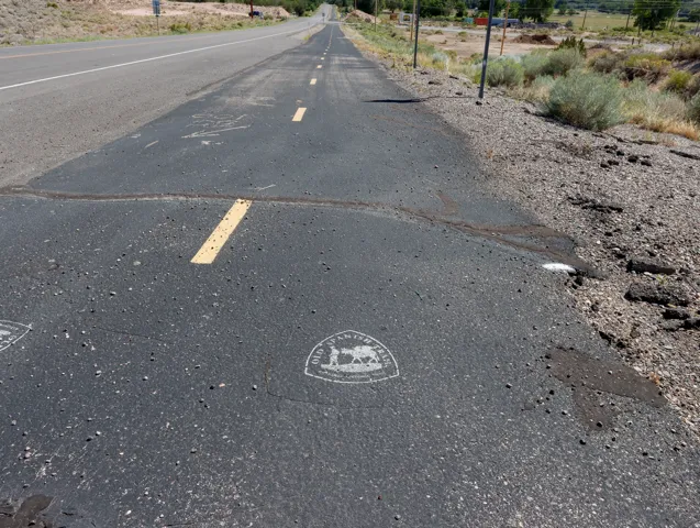 Paved road surface featuring a yellow dashed line, gravel shoulder, and a distant road extending into the landscape