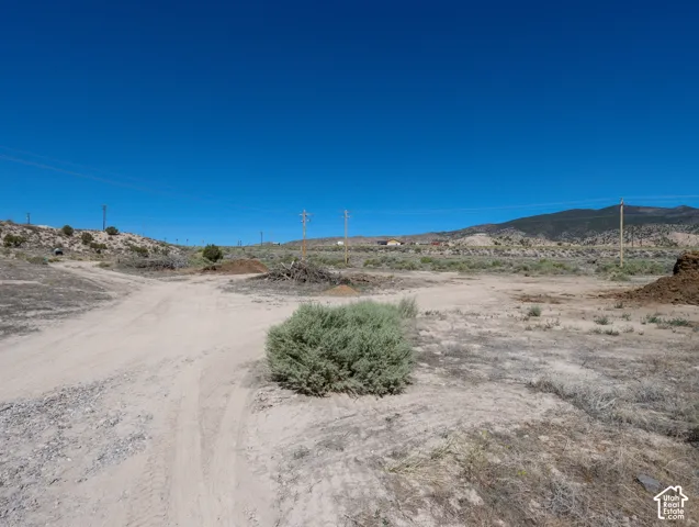 Expansive land parcel featuring a dirt path, natural vegetation, and distant mountain topography under a clear sky