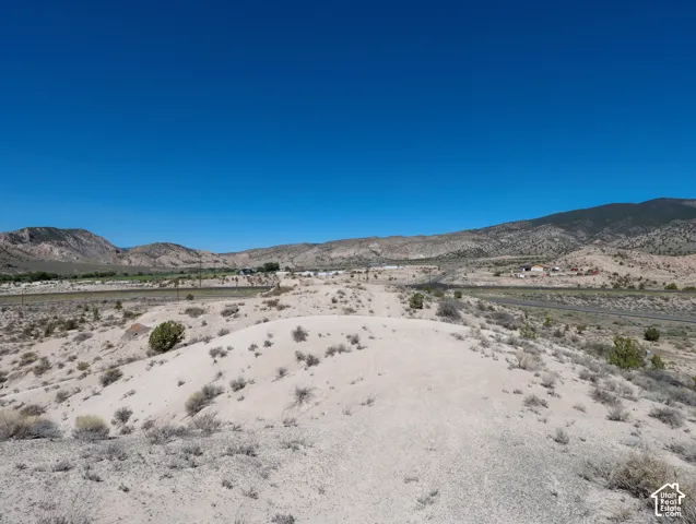 Expansive undeveloped land featuring rolling hills, sparse desert vegetation, distant mountains, and clear blue skies