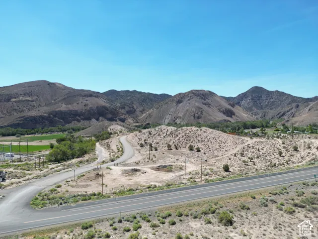 Expansive landscape featuring desert terrain with distant mountains, a paved highway, and a winding road