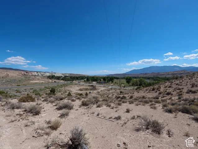 Expansive desert landscape featuring natural brush, distant mountains, and a clear blue sky