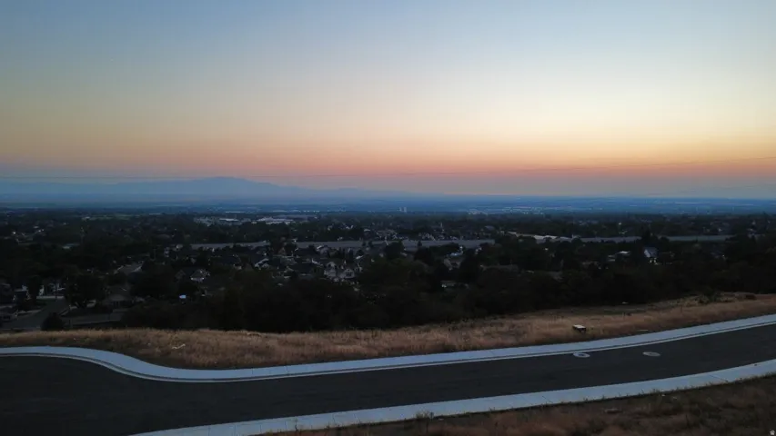 Paved road and sidewalk with expansive distant cityscape and mountain range under a colorful sky