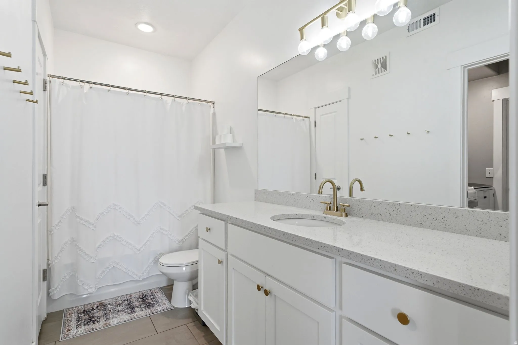 Bathroom featuring a white vanity with white shaker-style cabinetry, a speckled countertop, a gold-toned faucet, and a large wall-mounted mirror