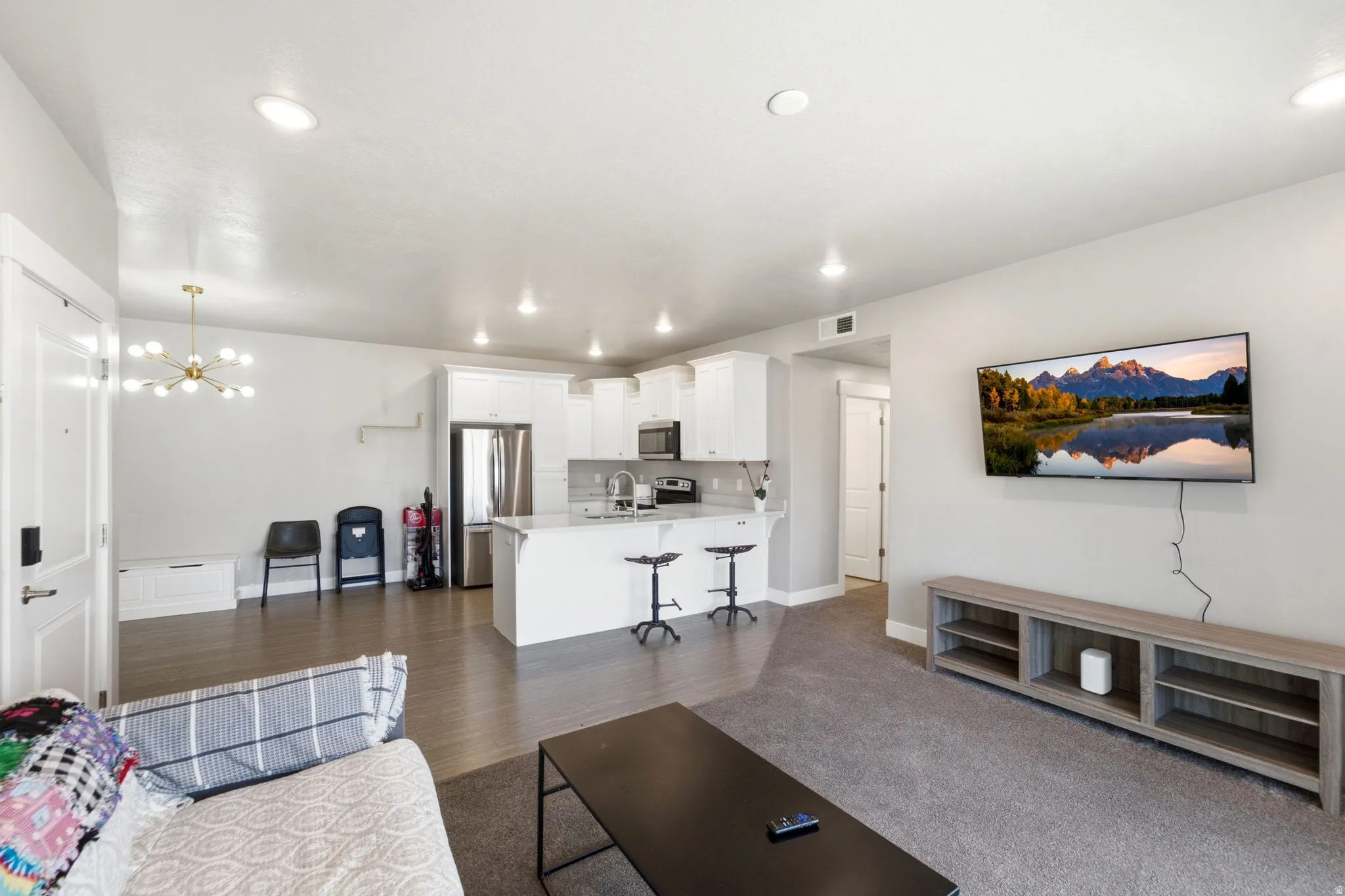 Open-concept living area featuring a kitchen with white cabinetry and a breakfast bar, stainless steel appliances, recessed lighting, and wood-finish flooring