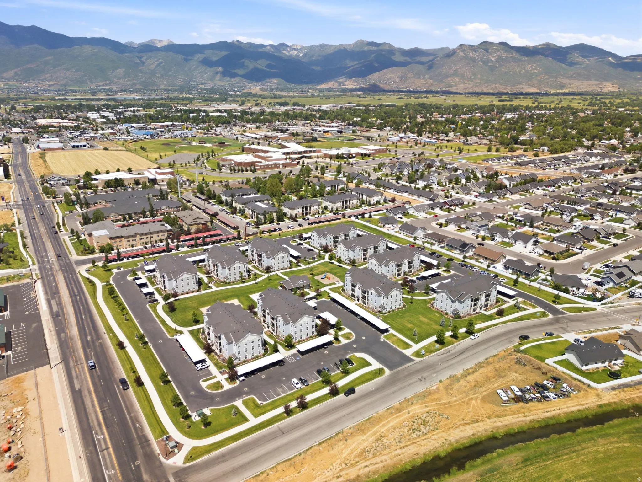 Expansive aerial showing a residential community with multi-story buildings, numerous single-story homes, mountains forming a dramatic backdrop, and paved roads