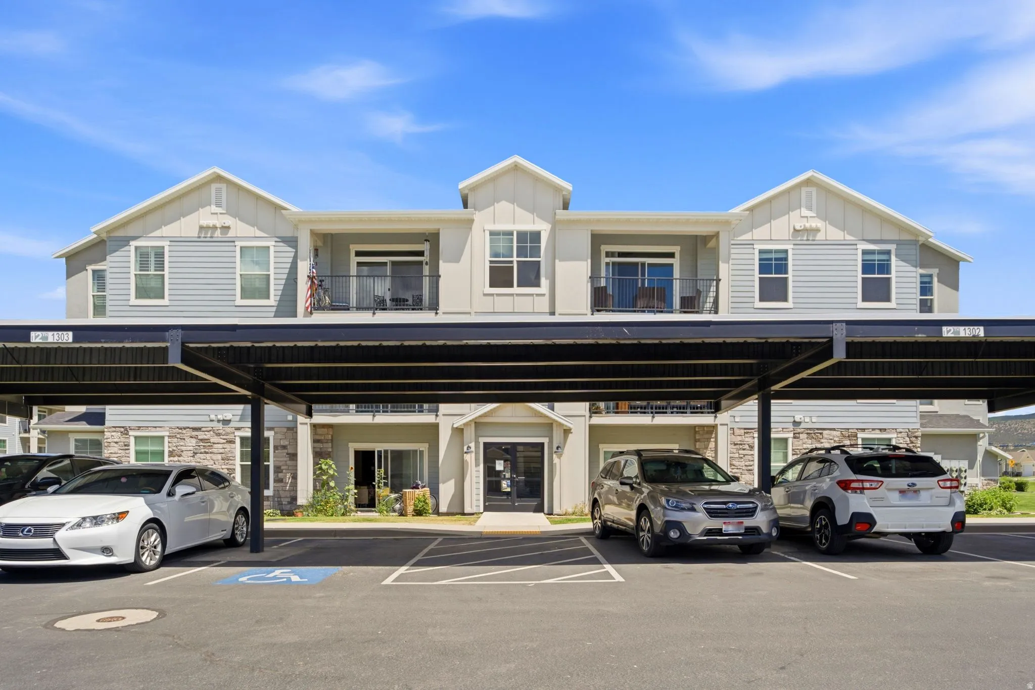 Multi-level residential building featuring covered parking, stone accents, and private balconies with black railings