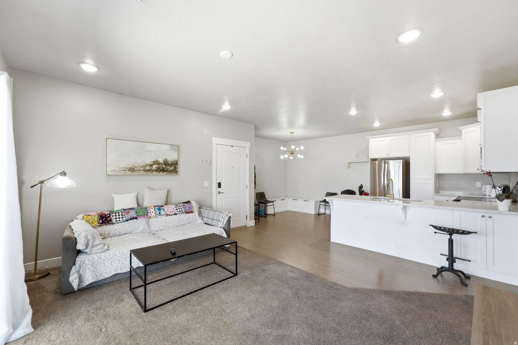 Open-concept living space featuring a combination of carpeting and wood-finish flooring, recessed lighting, and a kitchen with white cabinetry and stainless steel appliances