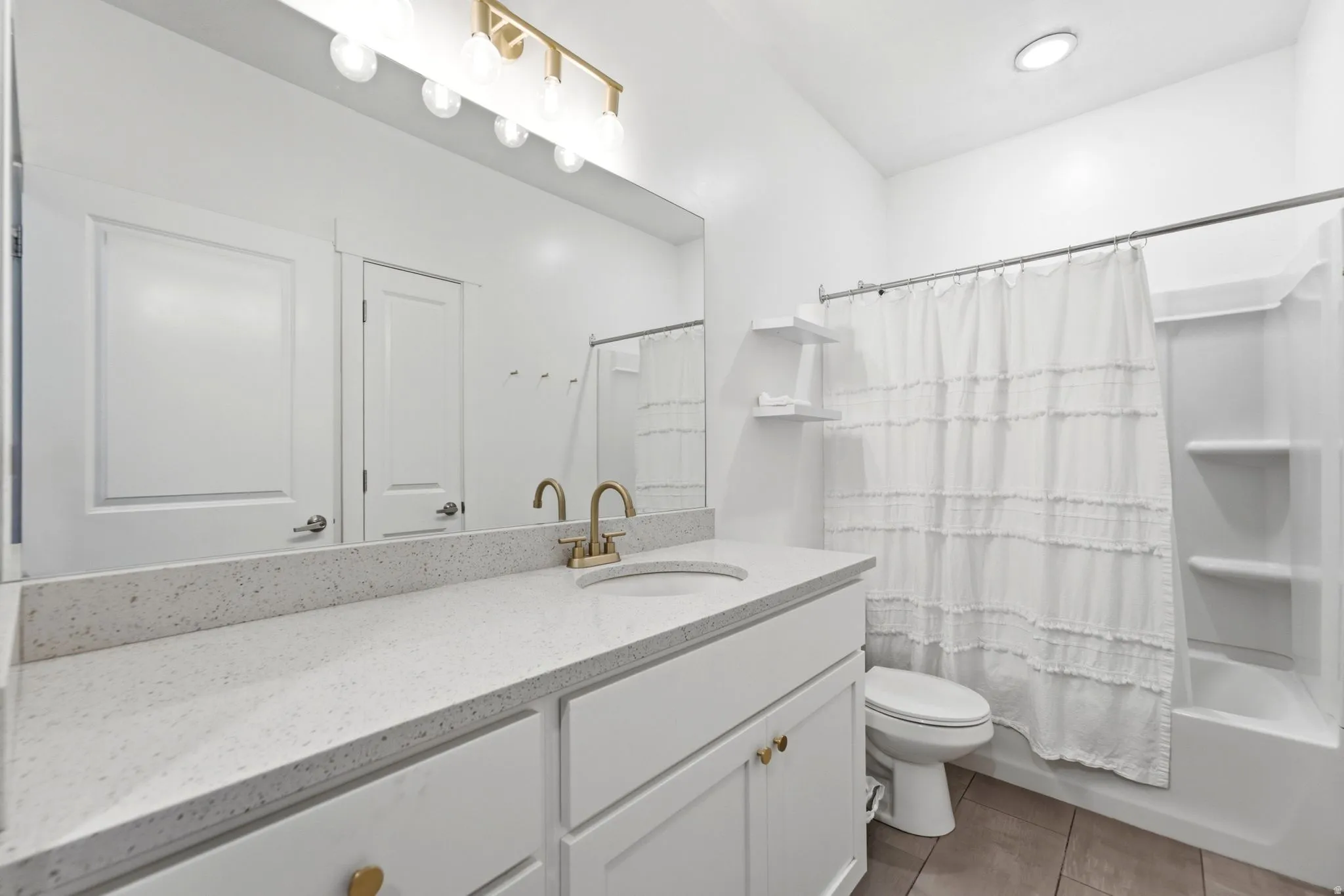 Bathroom featuring a white vanity with gold-tone hardware, a light-toned countertop, a gold-tone faucet, a large mirror, and a white tub/shower combination