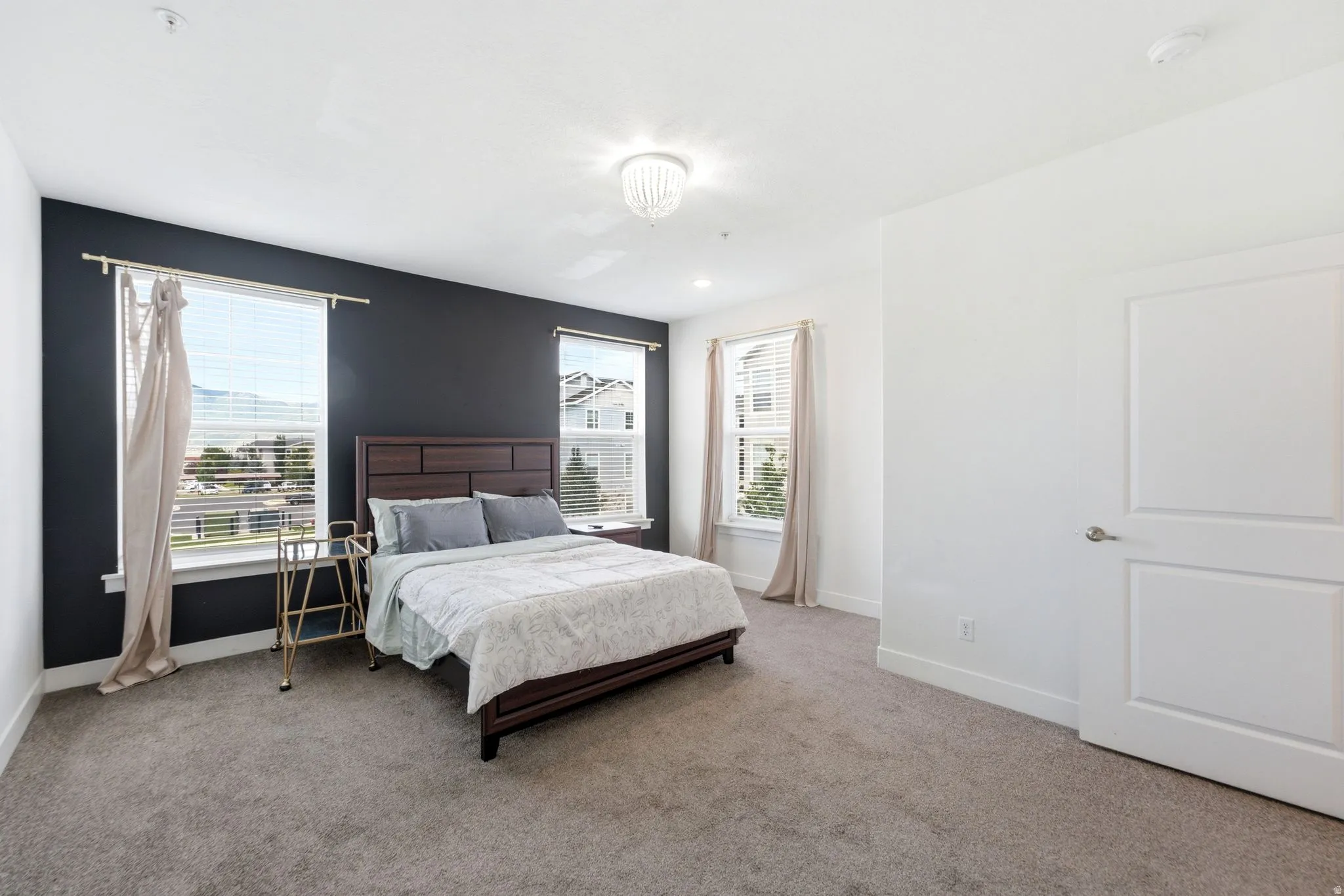 Spacious room featuring neutral carpet flooring, a decorative chandelier, and two windows with blinds and curtain rods