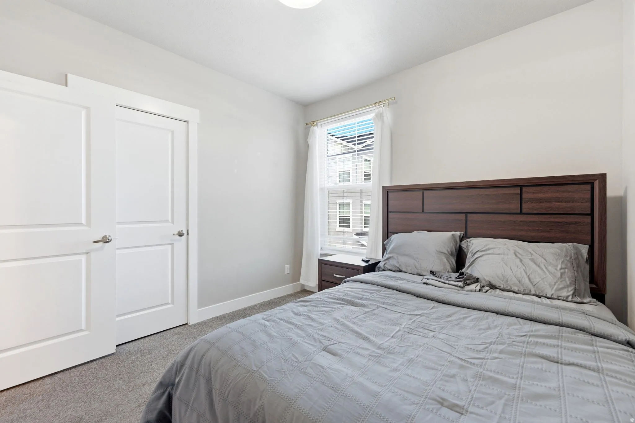 Bedroom featuring soft gray carpeting, white painted walls, and a window with blinds