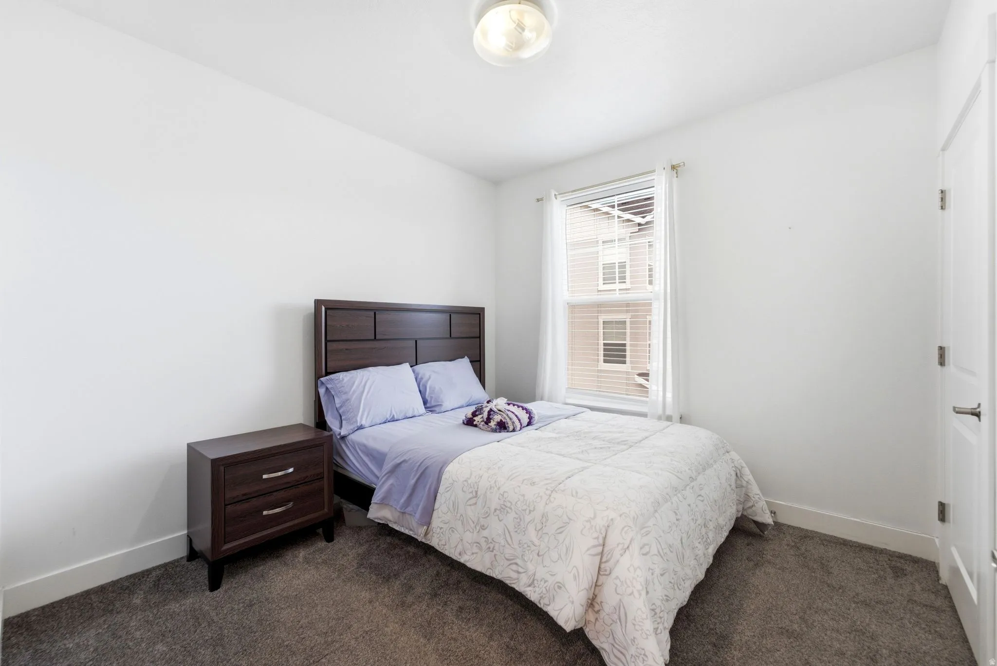 Room featuring a single window with blinds and white drapes, white walls, and dark gray carpeting
