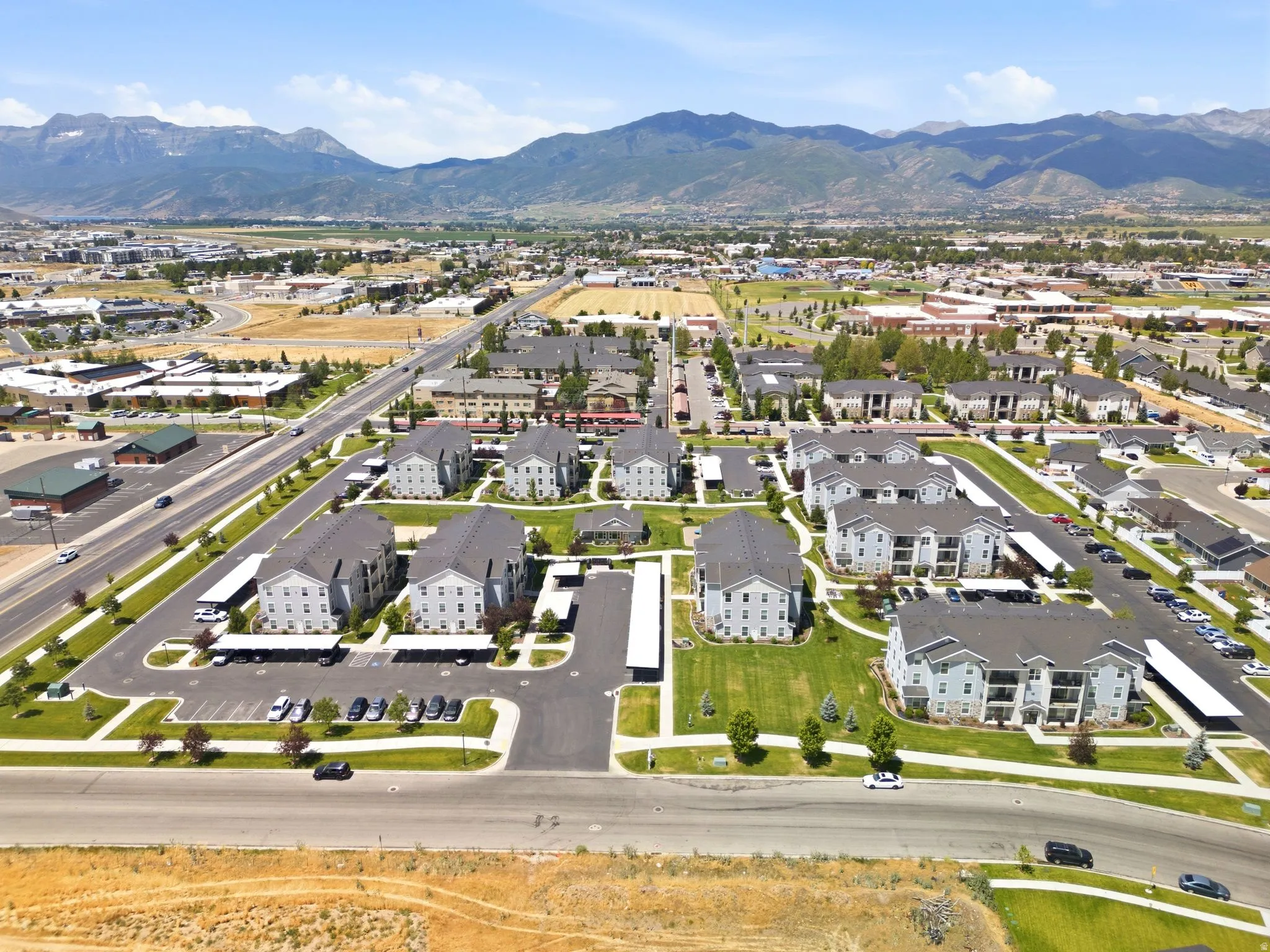 Community aerial showcasing multiple multi-story buildings with pitched roofs, covered parking structures, and landscaped green spaces