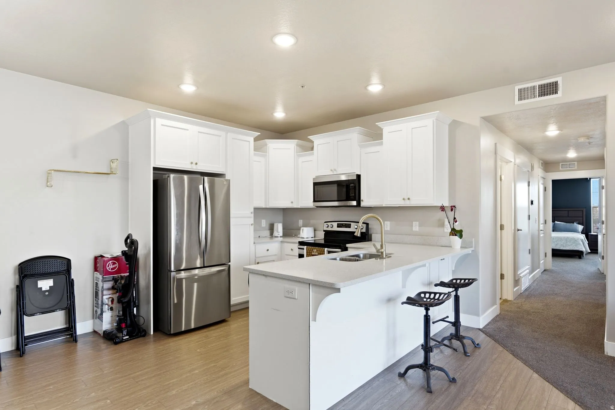 Open-concept kitchen featuring white shaker cabinetry, stainless steel appliances, a white countertop island with seating, and wood-finish flooring
