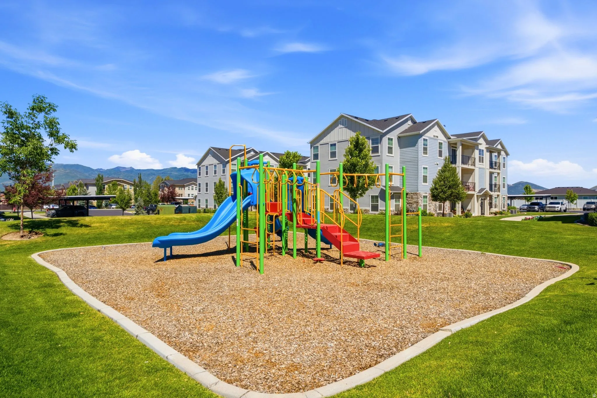 Community playground featuring a colorful playset with slides, ladders, and climbing structures, set on wood chip surfacing