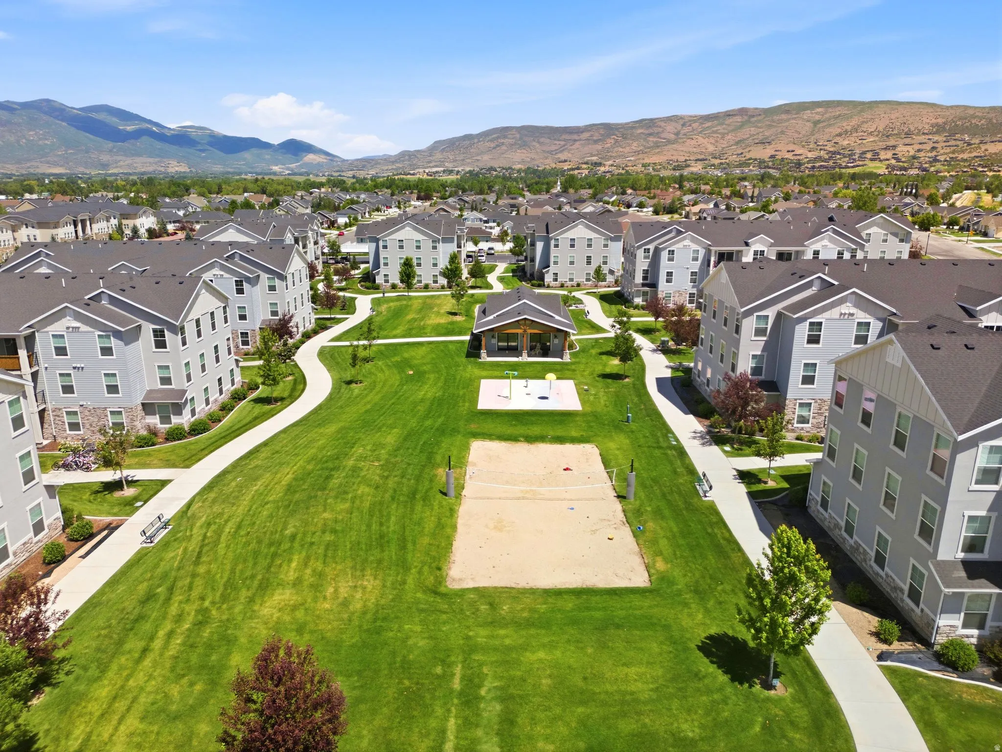 Central green space featuring a sand volleyball court, covered pavilion, and integrated play equipment