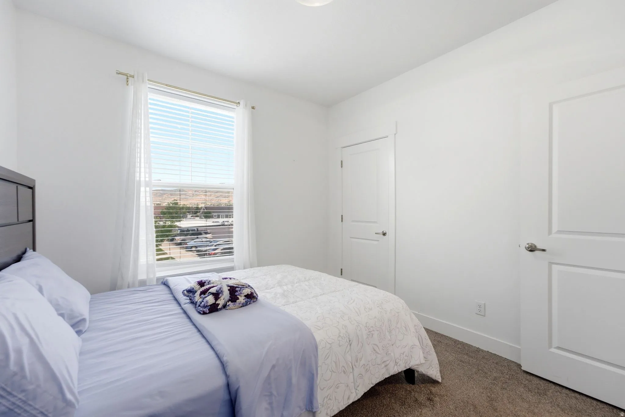 Bedroom featuring light-toned carpeting, white walls, and a window with horizontal blinds