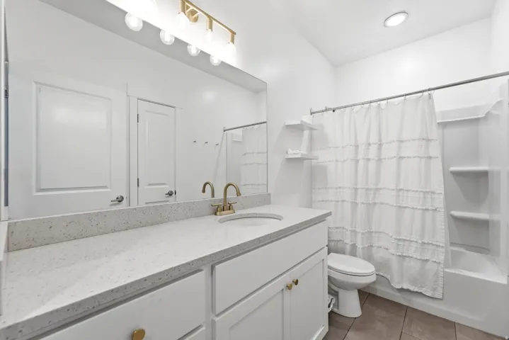 Bathroom featuring a white vanity with gold-tone hardware, a light-toned countertop, a gold-tone faucet, a large mirror, and a white tub/shower combination