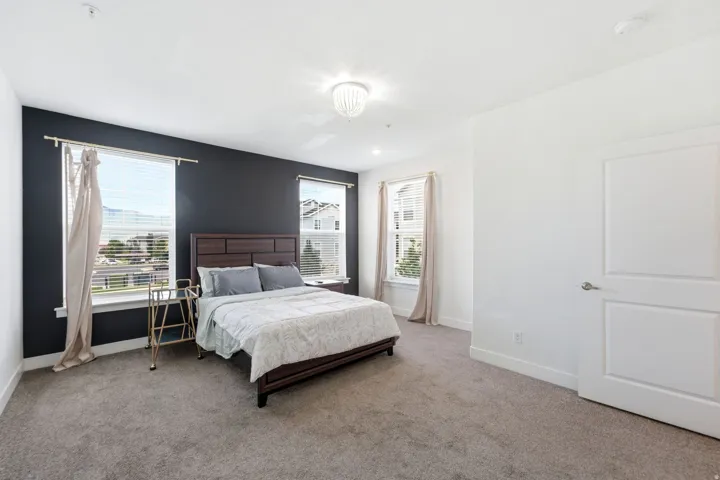 Spacious room featuring neutral carpet flooring, a decorative chandelier, and two windows with blinds and curtain rods