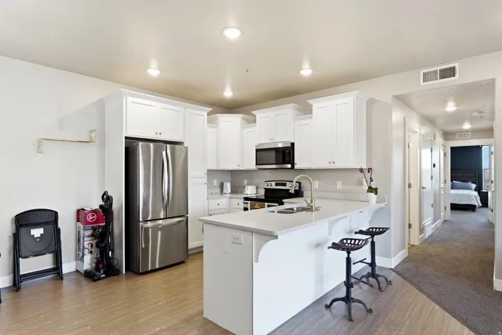 Open-concept kitchen featuring white shaker cabinetry, stainless steel appliances, a white countertop island with seating, and wood-finish flooring