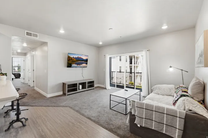 Spacious living area featuring carpet flooring, recessed lighting, and a sliding glass door opening to an exterior balcony