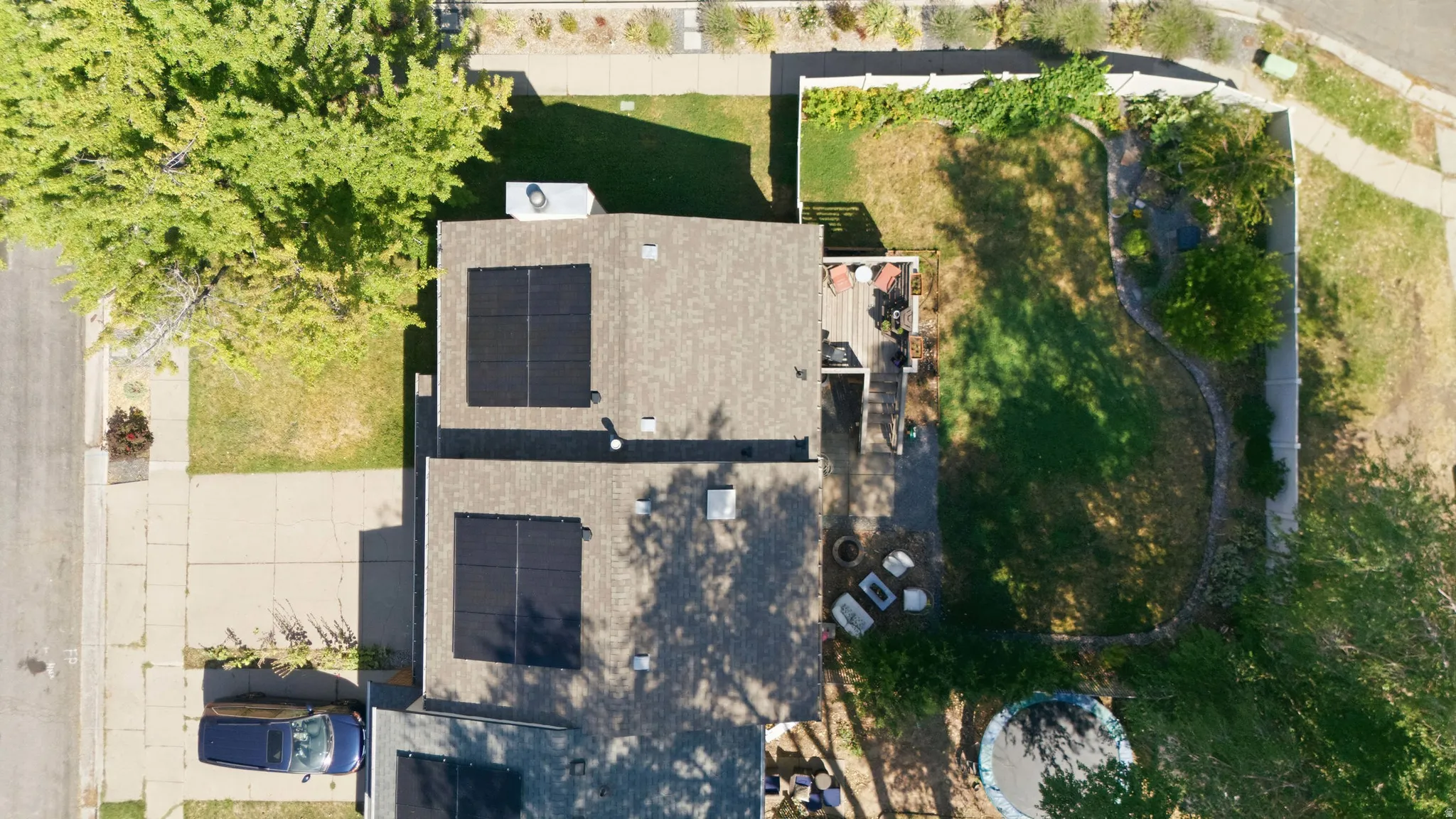 Aerial view showcasing a property with a shingle roof, two distinct solar panel arrays, and a rear deck