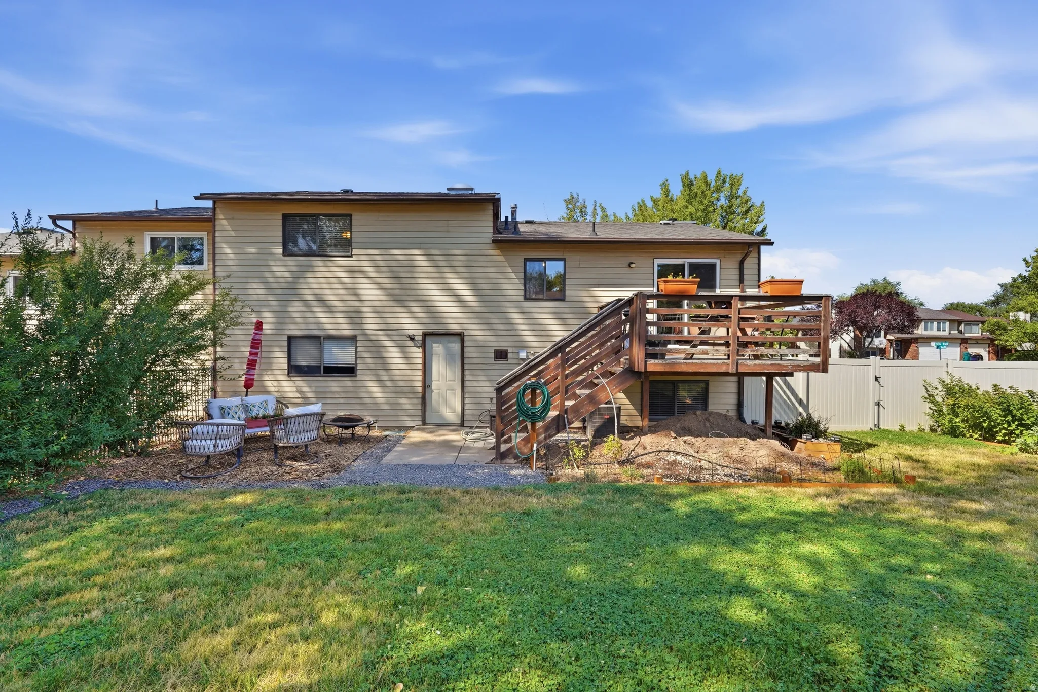 Expansive backyard featuring a wood deck with stairs, a patio area, and a large green lawn