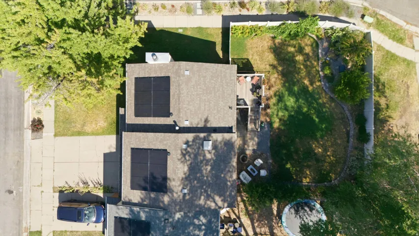 Aerial view showcasing a property with a shingle roof, two distinct solar panel arrays, and a rear deck