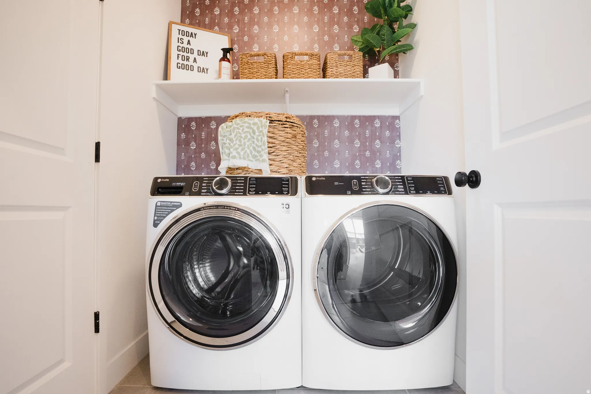 Dedicated laundry space featuring a side-by-side washer and dryer, an overhead shelf, and patterned accent wall