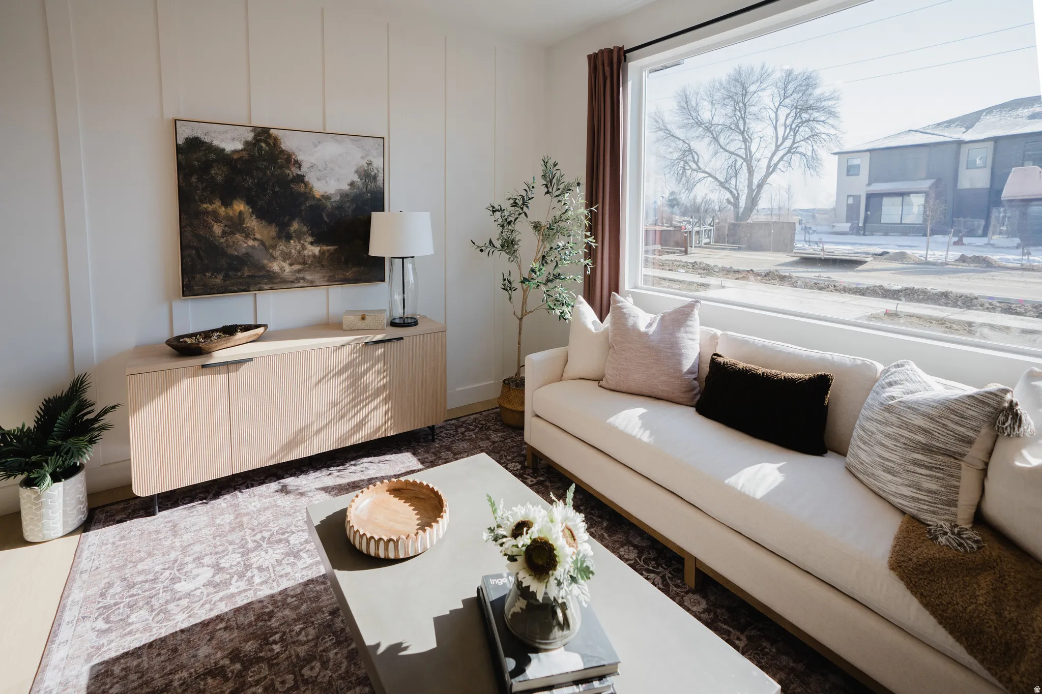Bright living space featuring a large picture window, board and batten accent wall, wood-finish flooring, and a large area rug