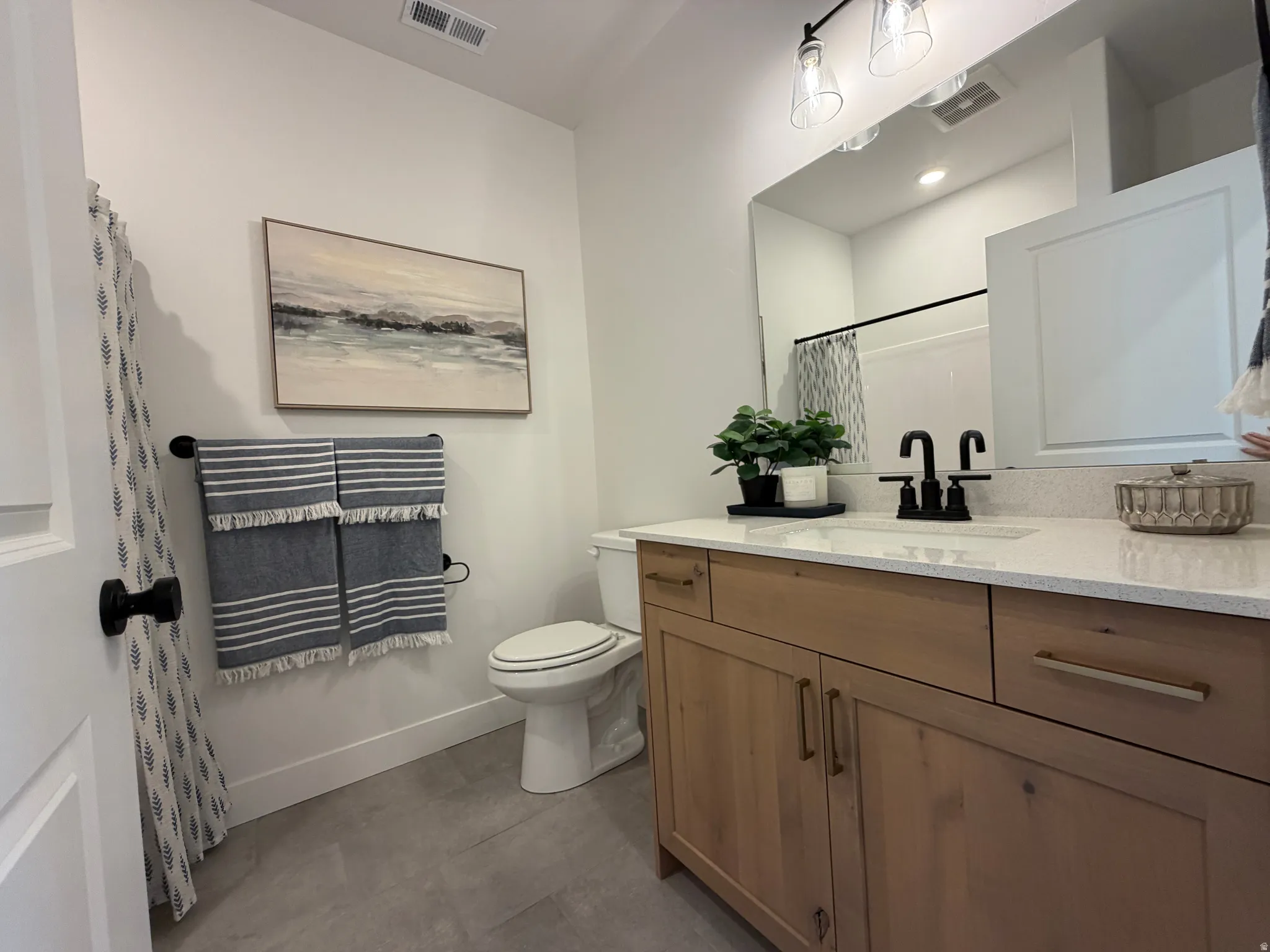Bathroom featuring a light wood-finish vanity with a quartz-style countertop, a rectangular undermount sink, and a black faucet