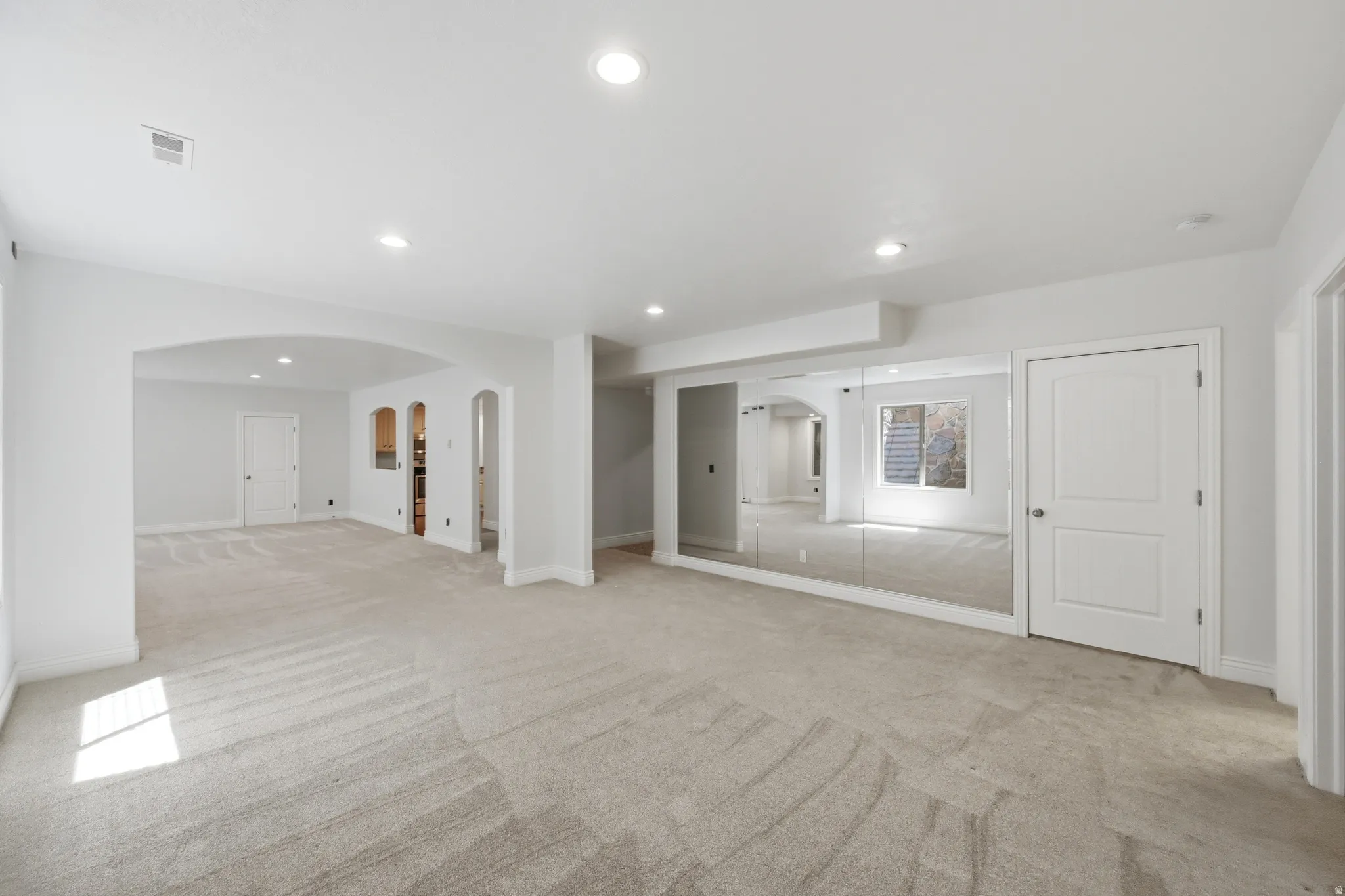 Open-concept lower level featuring neutral carpeting, recessed lighting, and a mirrored wall