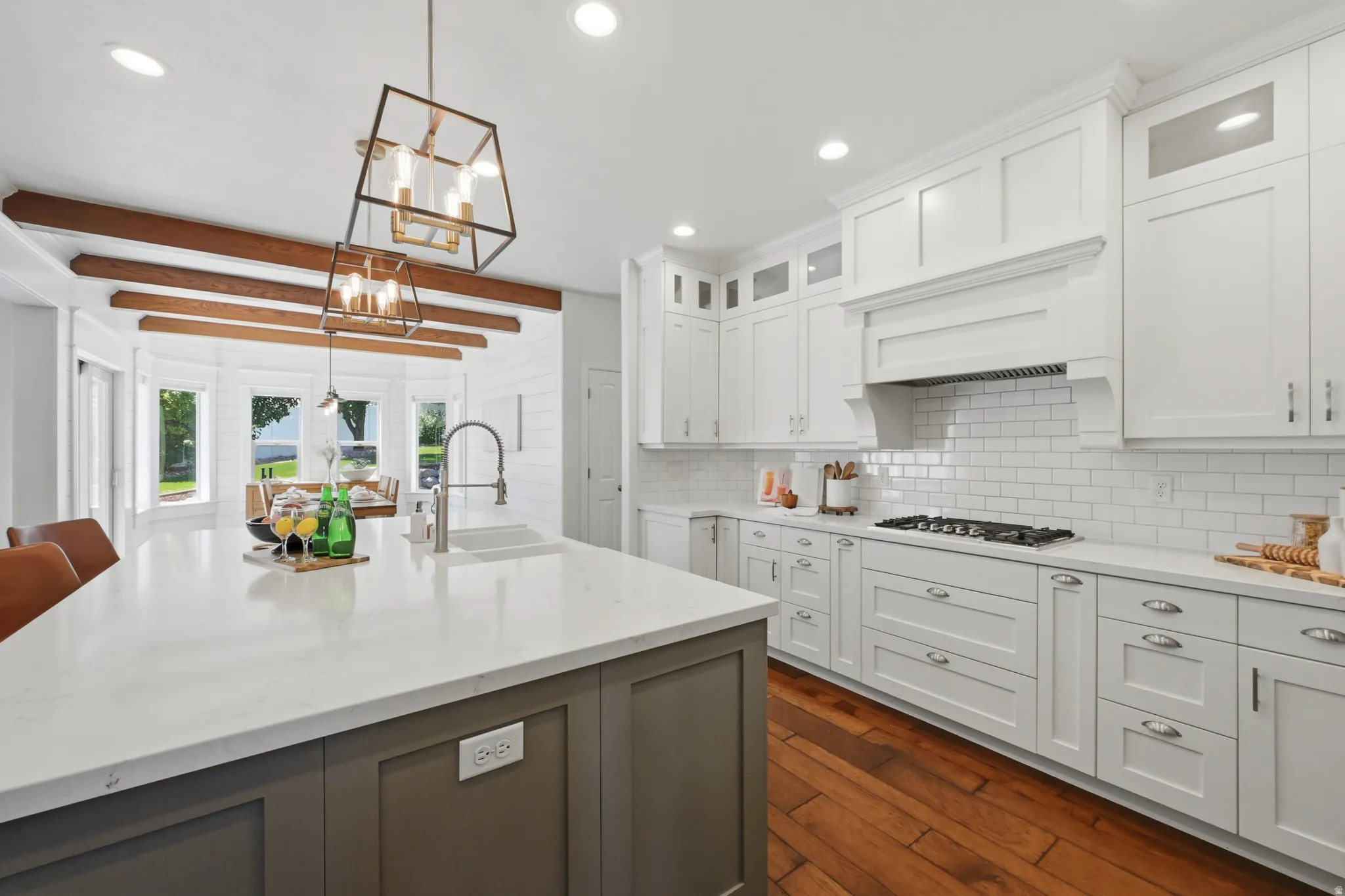 Spacious kitchen featuring a large island with a quartz countertop and integrated sink, white shaker cabinetry with brushed nickel hardware, subway tile backsplash, and wood-finish flooring