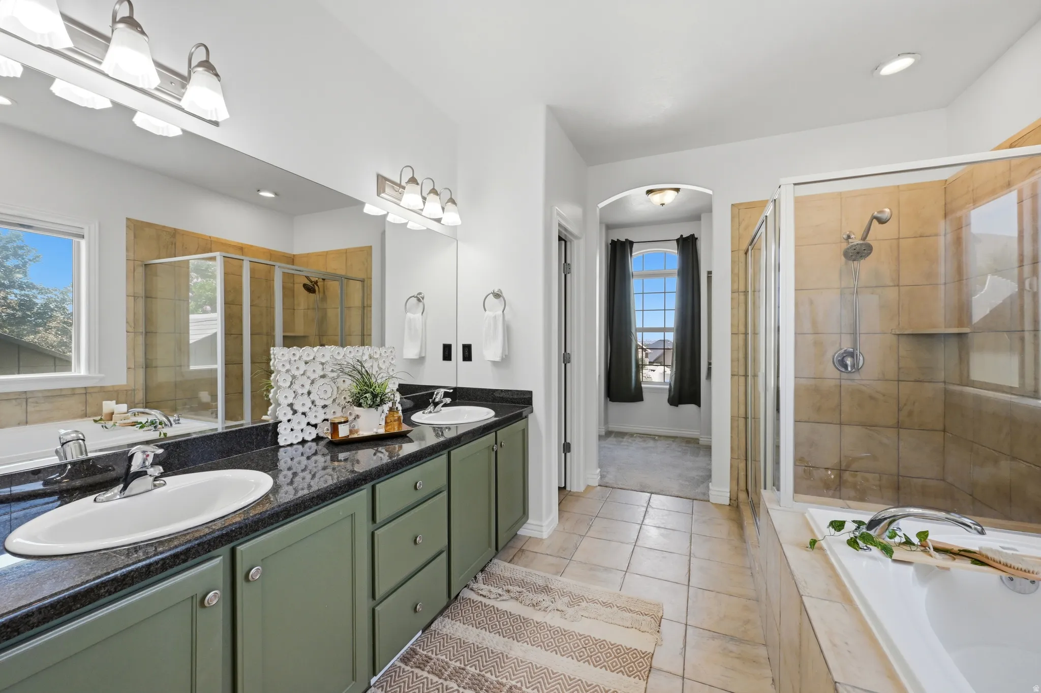 Dual vanity with dark countertops, a built-in soaking tub, and a separate glass-enclosed shower featuring tile surround