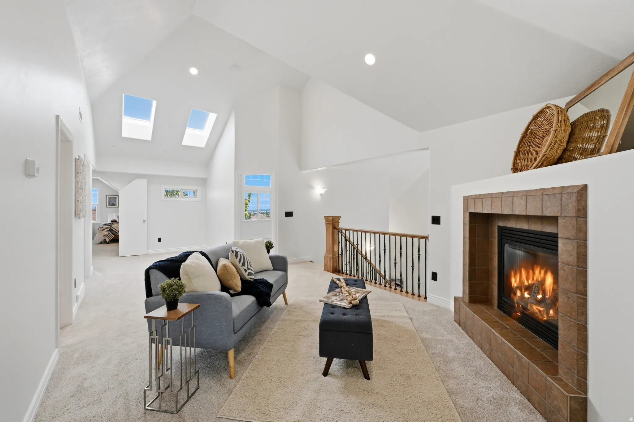 Vaulted ceilings with dual skylights illuminate this living area, featuring a tiled fireplace surround and a light-toned carpet