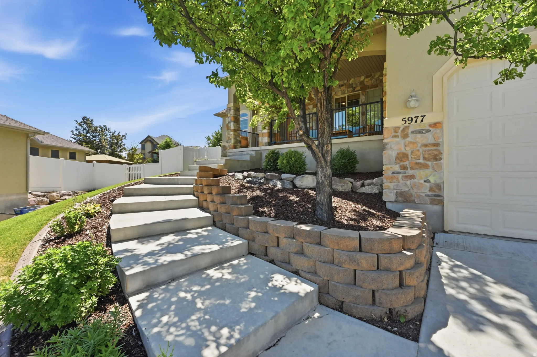 Concrete staircase entry with a stone retaining wall and mature landscaping