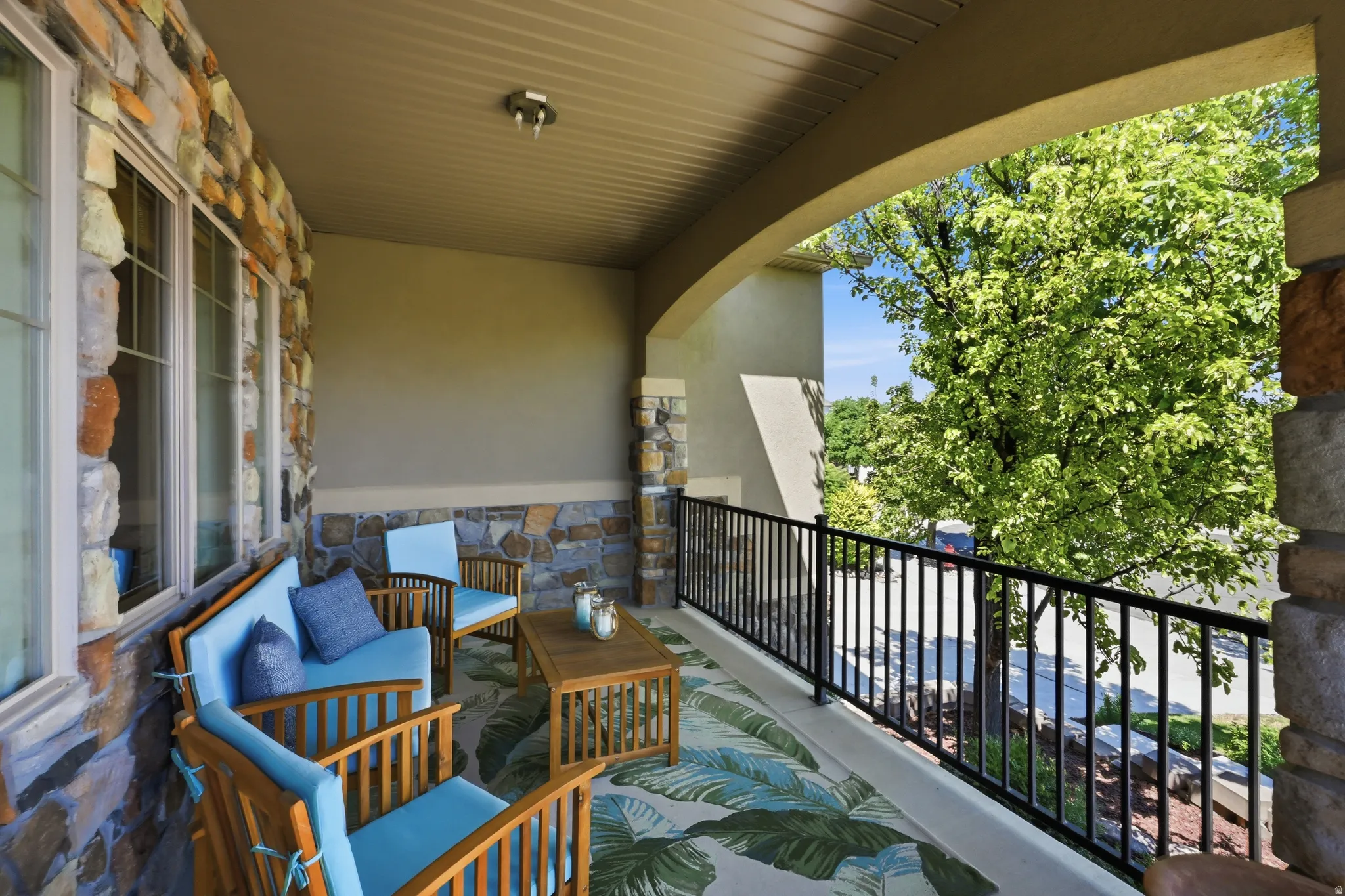Covered stone patio featuring a textured ceiling, expansive windows, and a black wrought iron railing