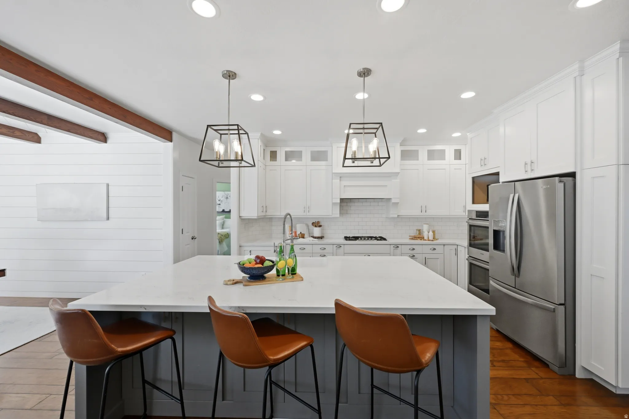 Spacious kitchen featuring a large central island with seating, pendant lighting, white shaker cabinetry, stainless steel appliances, and a subway tile backsplash