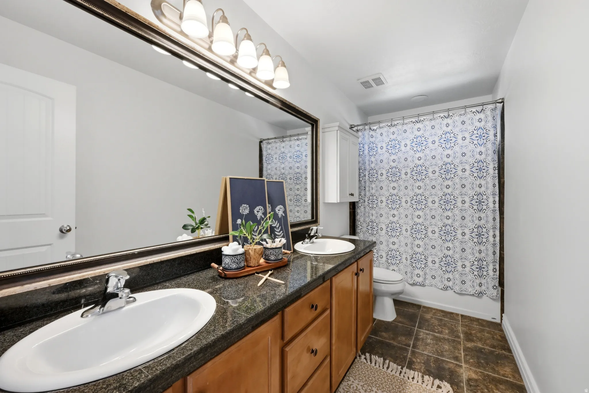 Bathroom featuring a spacious dual-sink vanity with a dark countertop and wood-finish cabinetry