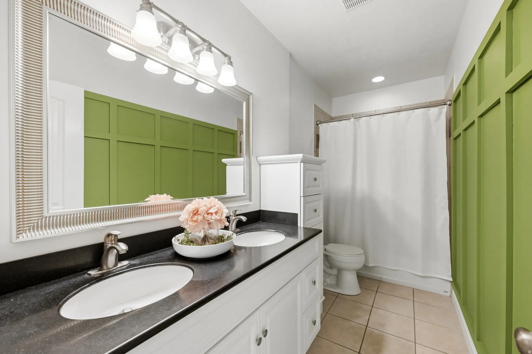Bathroom featuring a double vanity with undermount sinks, a dark countertop, and a framed mirror