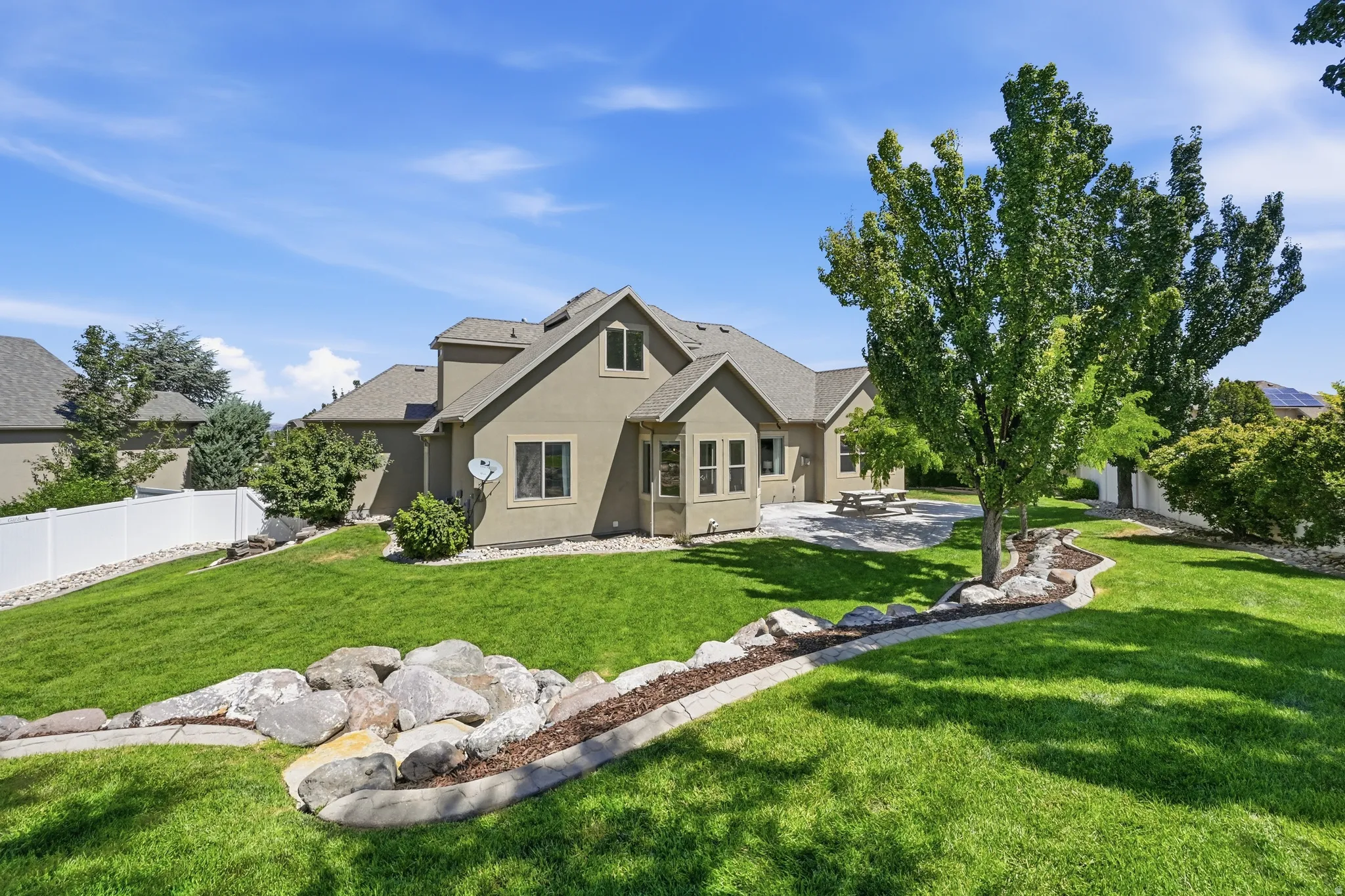 Expansive backyard featuring a manicured lawn, established landscaping, and a concrete patio