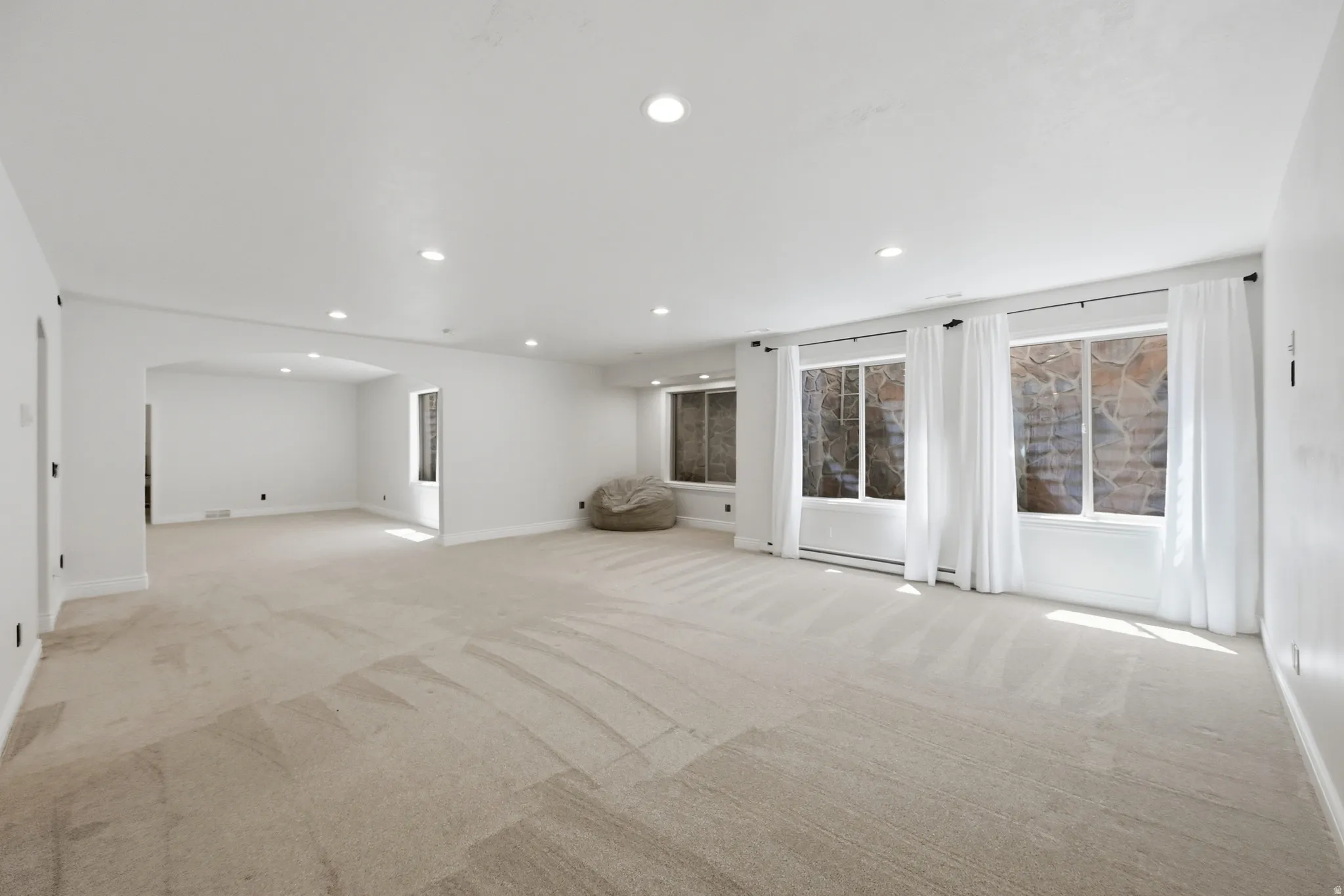 Spacious room featuring neutral carpeting, recessed lighting, white walls, and multiple windows with white trim and curtains