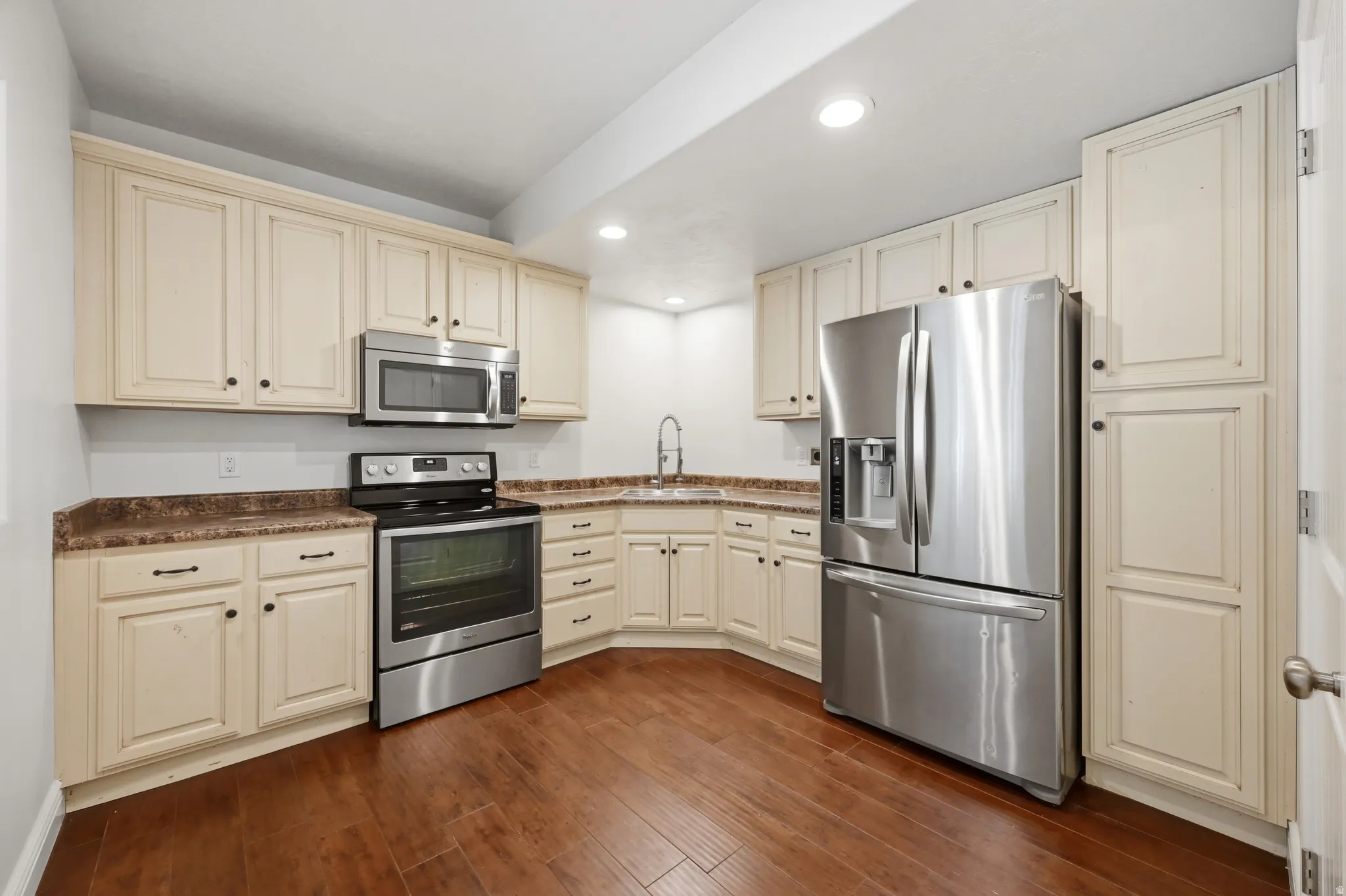 Kitchen featuring cream cabinetry, stainless steel appliances, wood-finish flooring, recessed lighting, and dark countertops