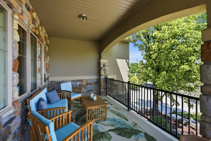 Covered stone patio featuring a textured ceiling, expansive windows, and a black wrought iron railing