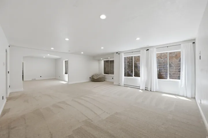 Spacious room featuring neutral carpeting, recessed lighting, white walls, and multiple windows with white trim and curtains