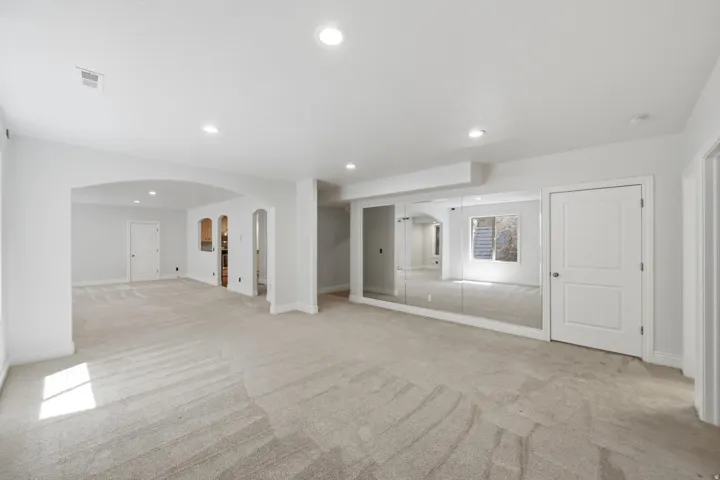 Open-concept lower level featuring neutral carpeting, recessed lighting, and a mirrored wall