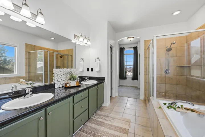 Dual vanity with dark countertops, a built-in soaking tub, and a separate glass-enclosed shower featuring tile surround