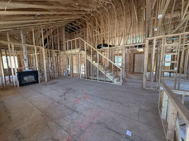 Spacious residential interior framed for construction, featuring an integrated fireplace unit, an open-concept design, and a visible staircase leading to an upper level