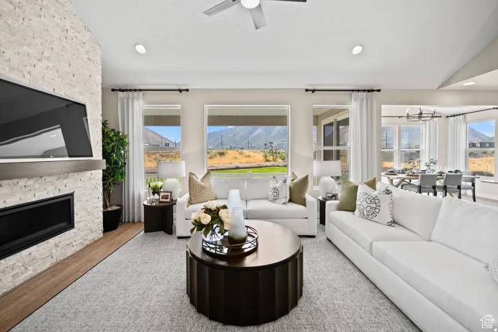Spacious living area featuring a stacked stone fireplace with a wood-finish mantel, recessed lighting, expansive windows, and wood-finish flooring