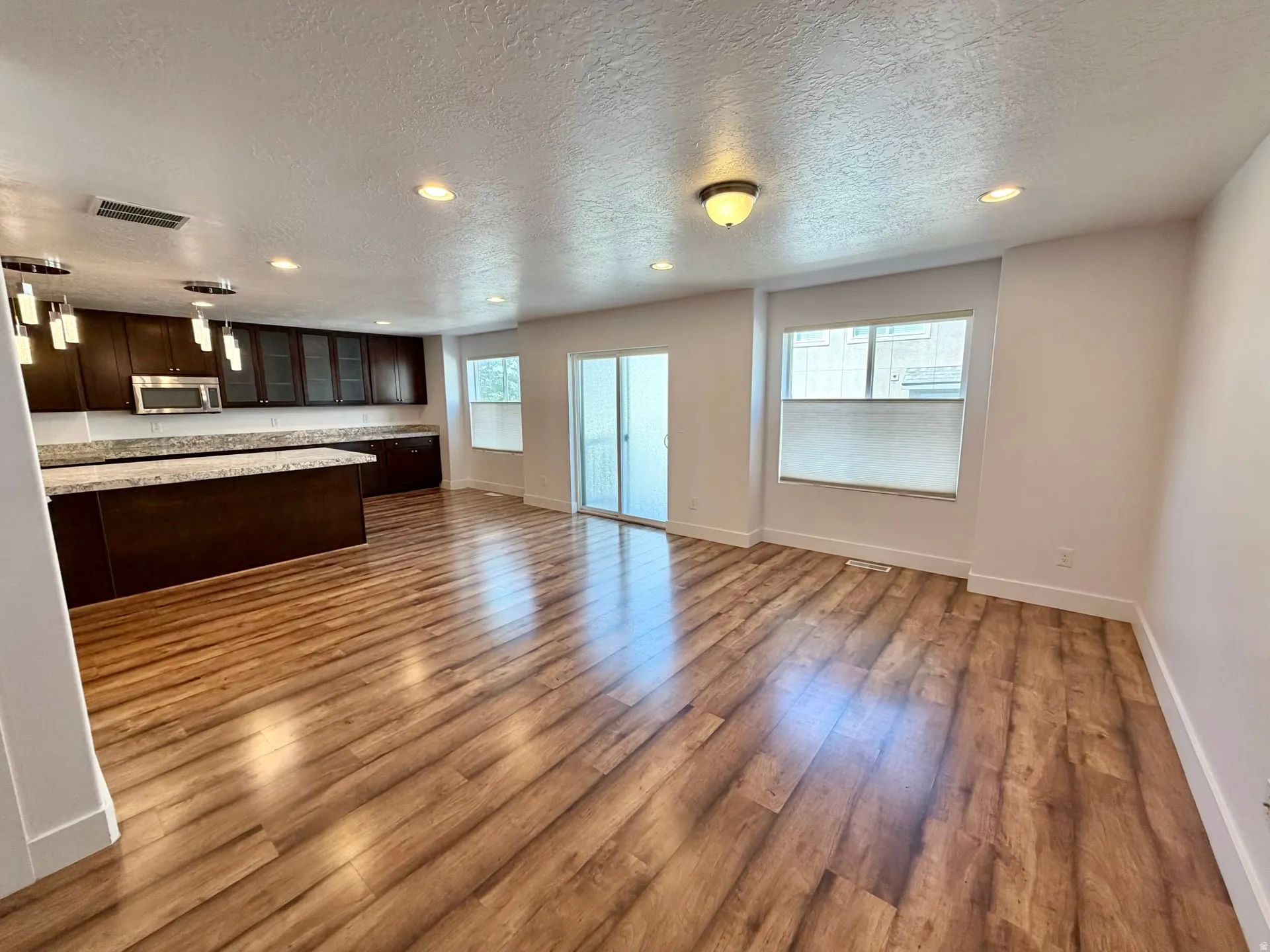 Open-concept living space with wood-finish flooring, recessed lighting, and a sliding glass door